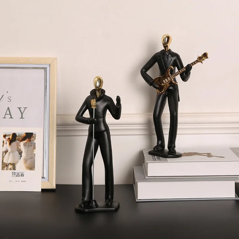 Black figures of a person playing guitar and another person waving on a shelf with books and a framed picture.