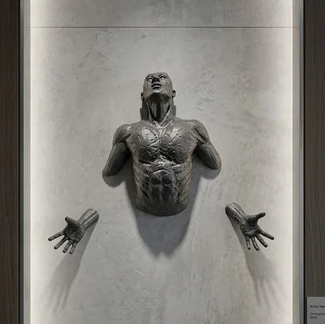 Bronze sculpture of a human figure on a plain wall