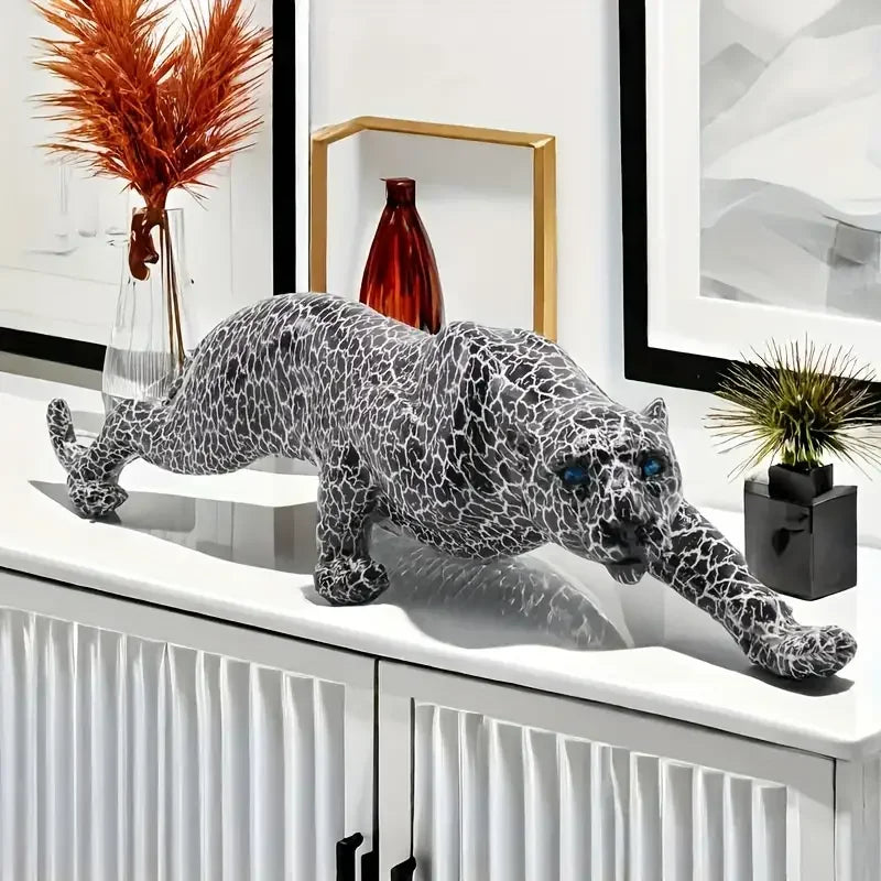Decorative leopard sculpture on a white surface with framed artwork and plants in the background.