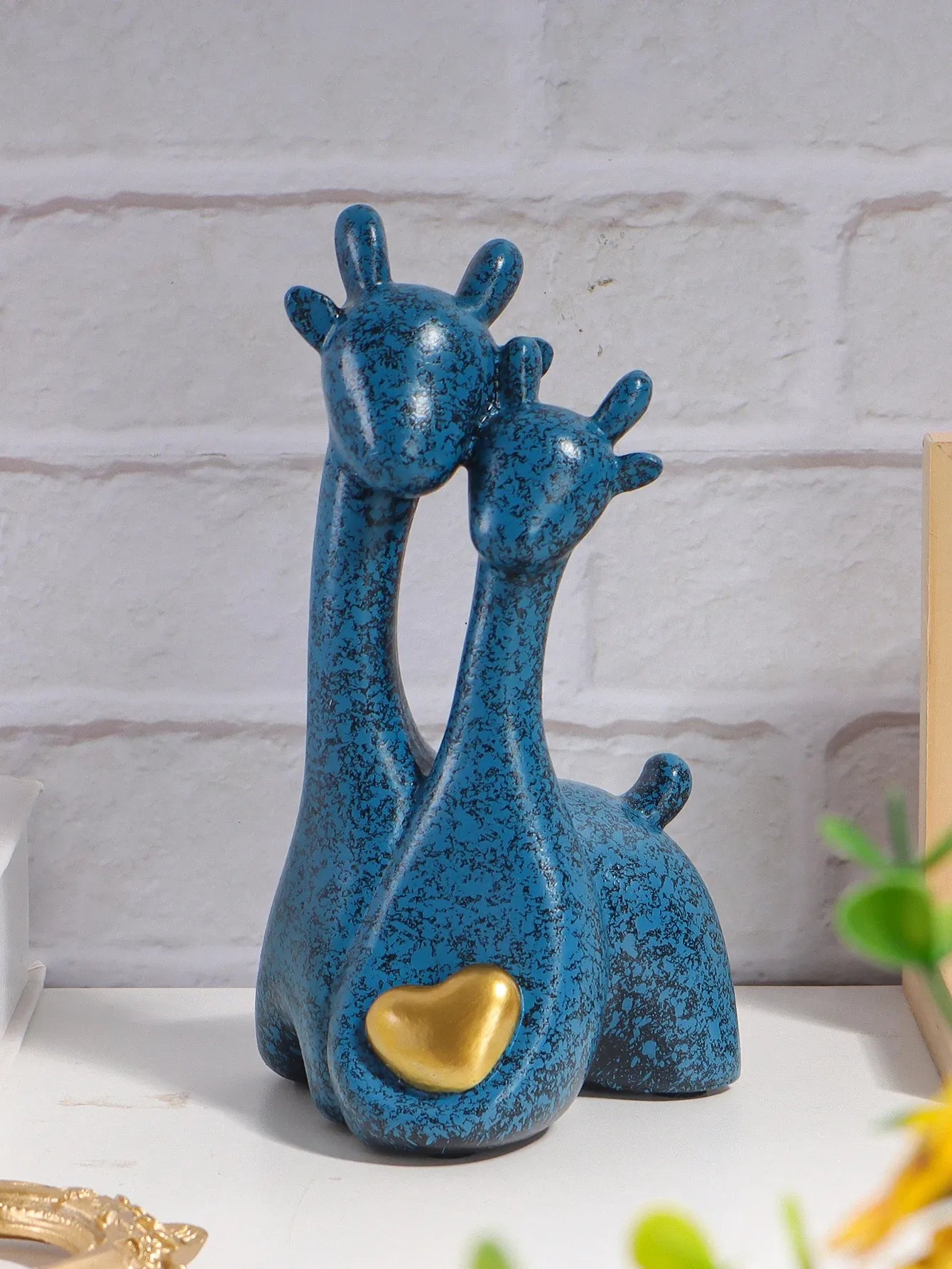 Blue ceramic giraffe figurine with a gold heart on a white surface.
