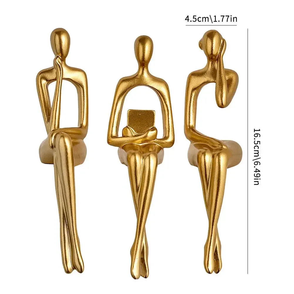 Three gold-colored sculptures of sitting figures with measurements on a white background