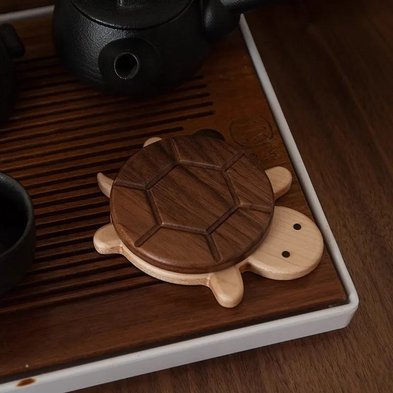 Wooden turtle-shaped coaster on a wooden tray with a teapot and cup in the background.