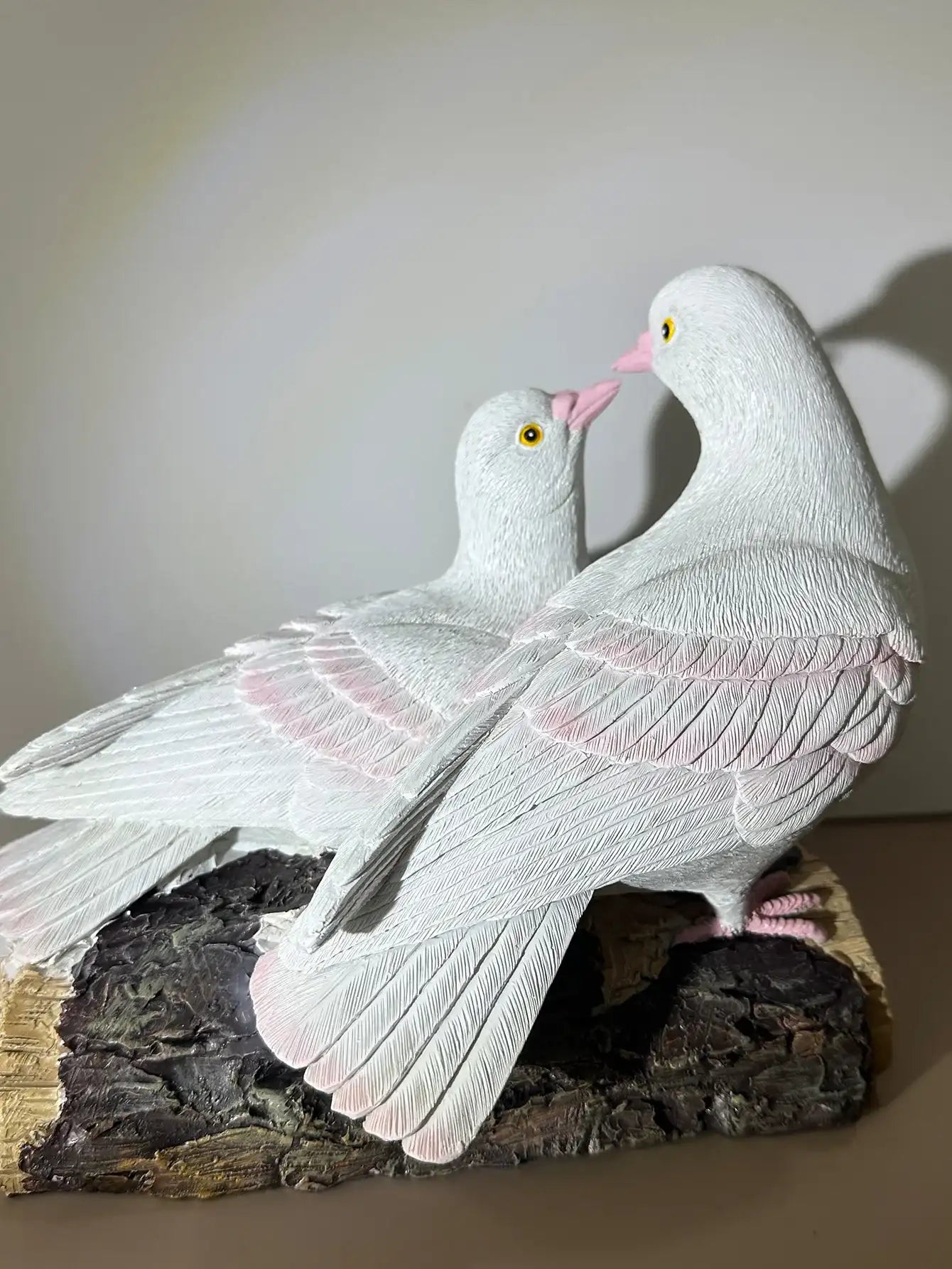 Two white doves with pink beaks on a dark base against a neutral background