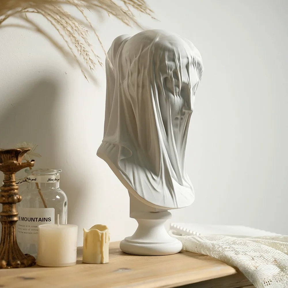 White marble bust draped with fabric on a wooden surface with decorative items.