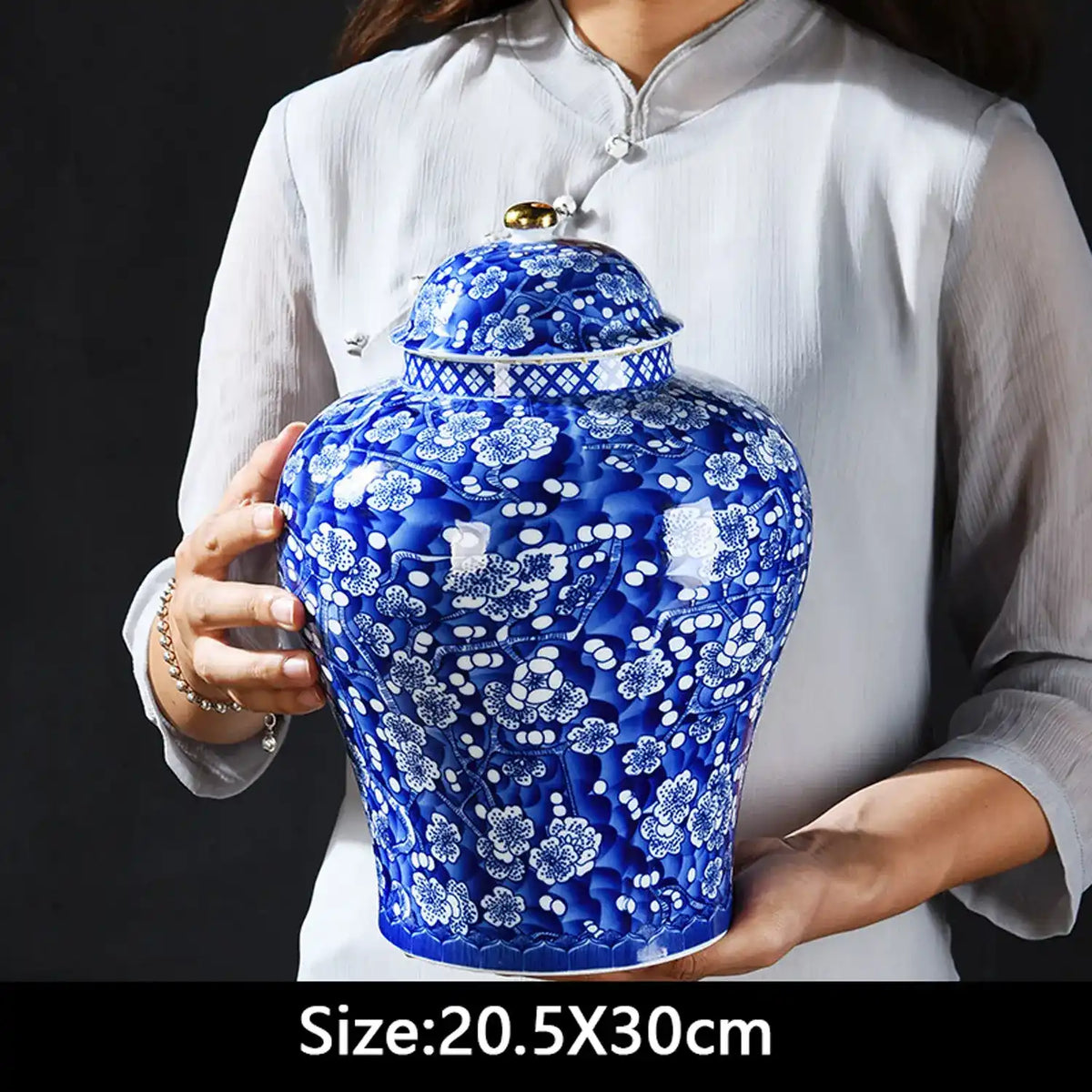 Person holding a blue and white ceramic jar with floral patterns on a black background