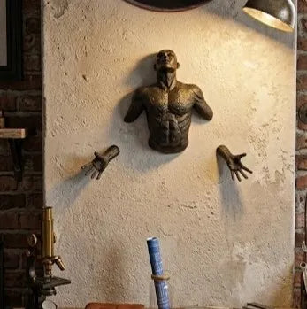 Bronze sculpture of a shirtless man on a textured wall with tools in the foreground.