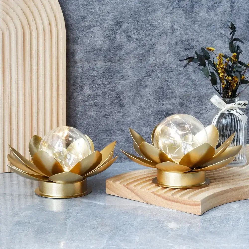 Two gold lotus-shaped lamps on a wooden stand with a gray wall and decorative elements in the background.