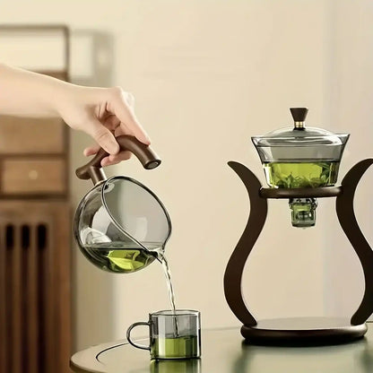  A Glass teapot with wooden handle being used to pour green tea into another glass container.