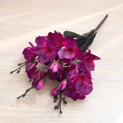 Artificial purple flower arrangement on a textured beige surface