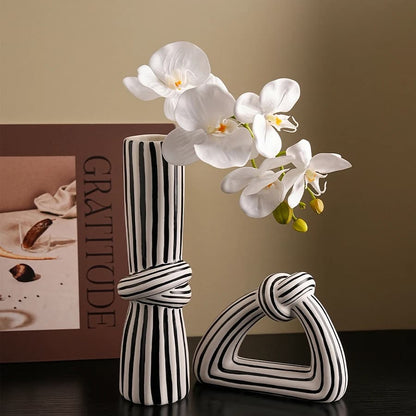 Black and white striped vases with a white orchid on a dark surface.