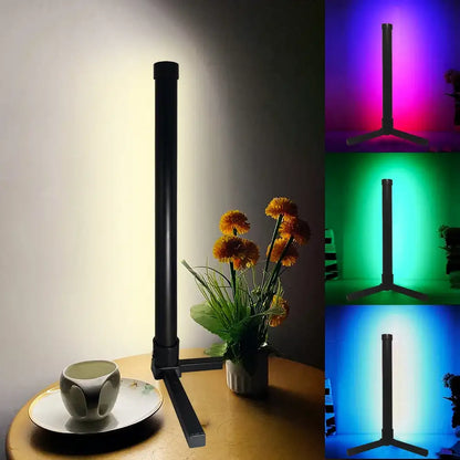 Black LED desk lamp with color-changing capabilities on a table with flowers and a cup.