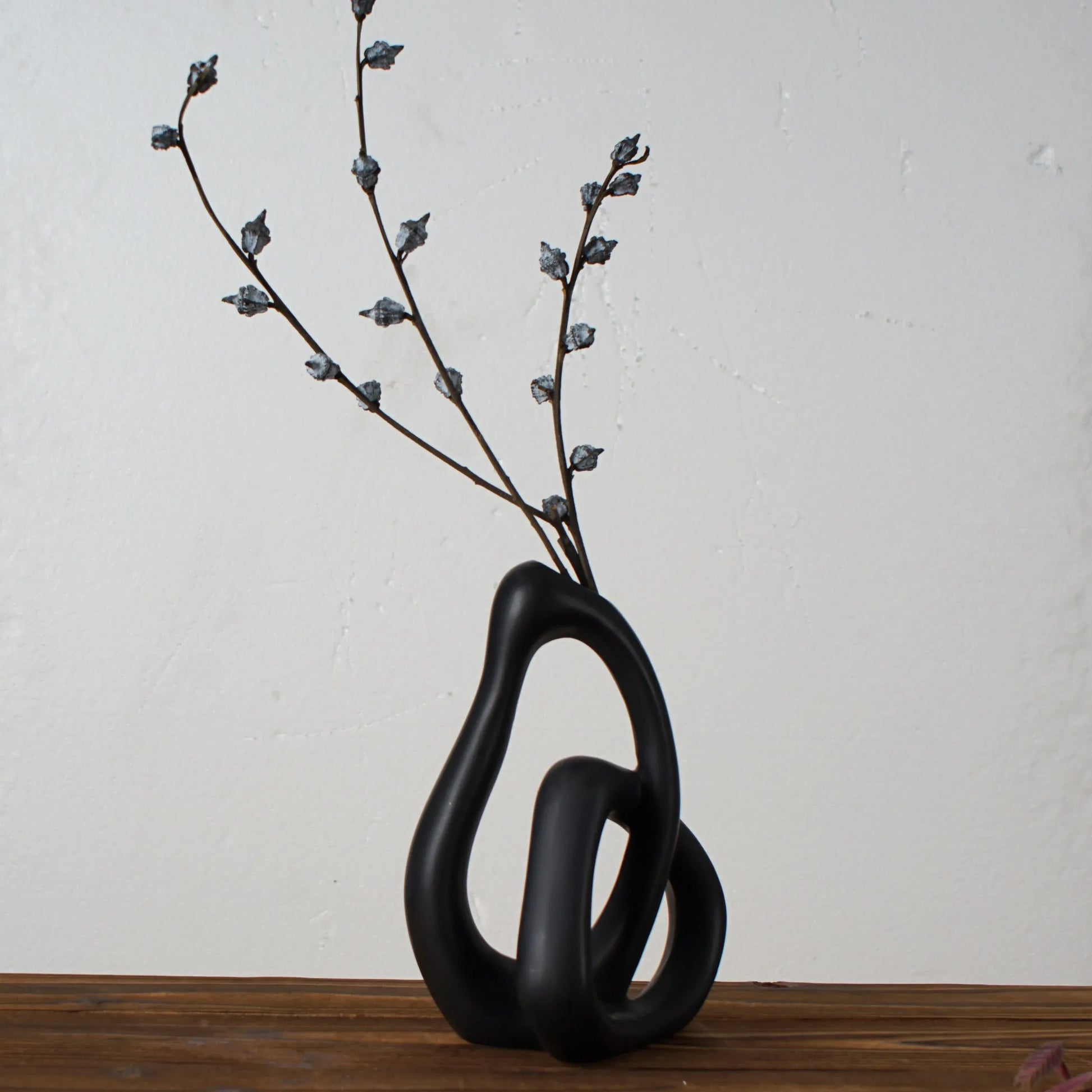Black abstract vase with branches on a wooden surface and light gray background