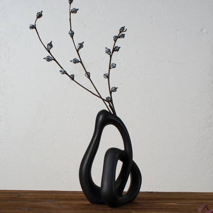 Black abstract vase with branches on a wooden surface and light gray background