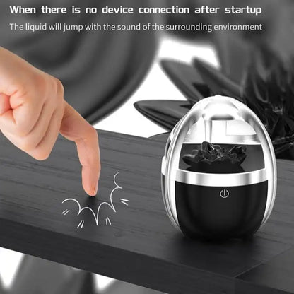 Black and silver Bluetooth speaker on a desk  on a wooden surface with a hand pointing at it.