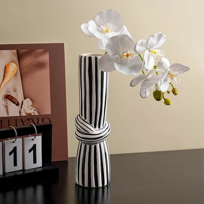 Black and white striped vase with white orchids on a wooden surface.