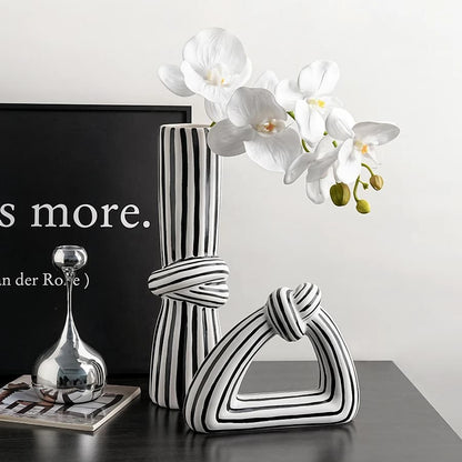 Black and white striped vase with a silver vase and white flowers on a dark surface.