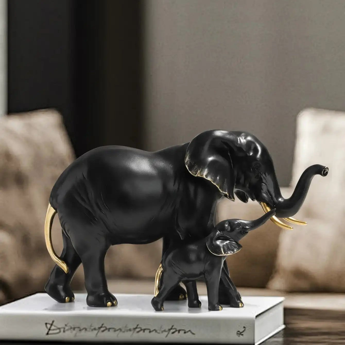 Black elephant figurine with a smaller one on a marble base, placed on a wooden surface.