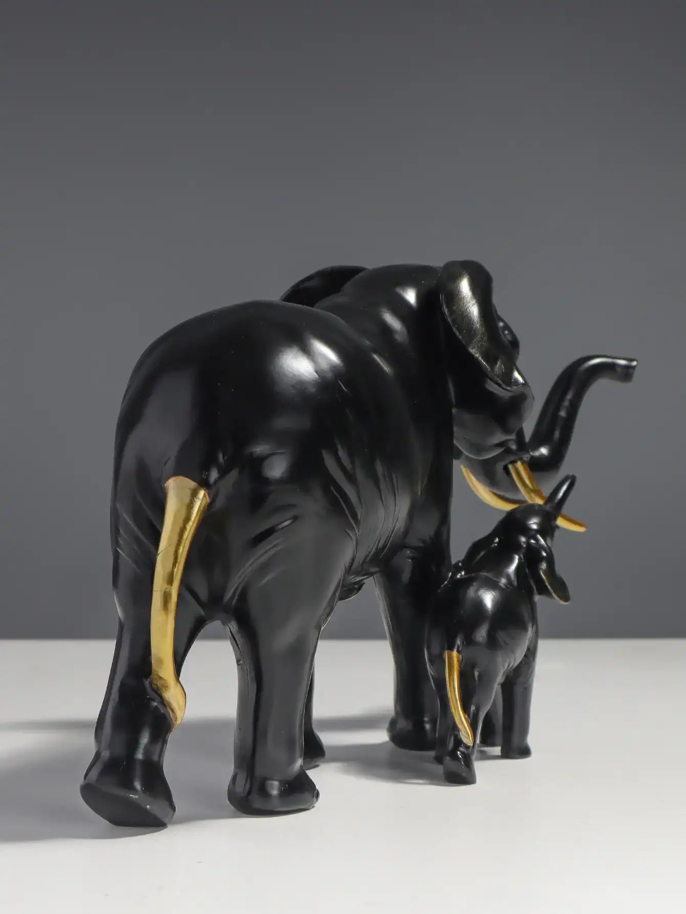 Black elephant figurine with a smaller elephant on its back against a gray background