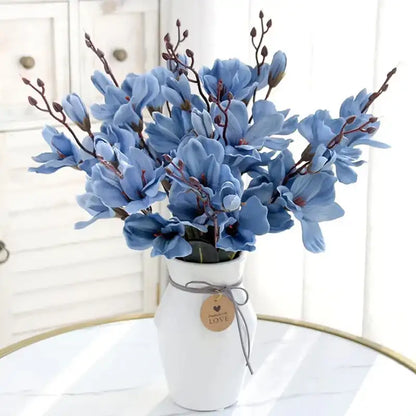 Blue flowers in a white vase with a 'LOVE' tag on a white surface.