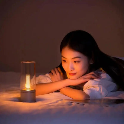 Woman lying on a bed next to a lit candle in a glass holder, surrounded by soft lighting.