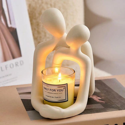Ceramic sculpture of two figures holding a lit candle labeled 'Only For You' on a wooden surface.
