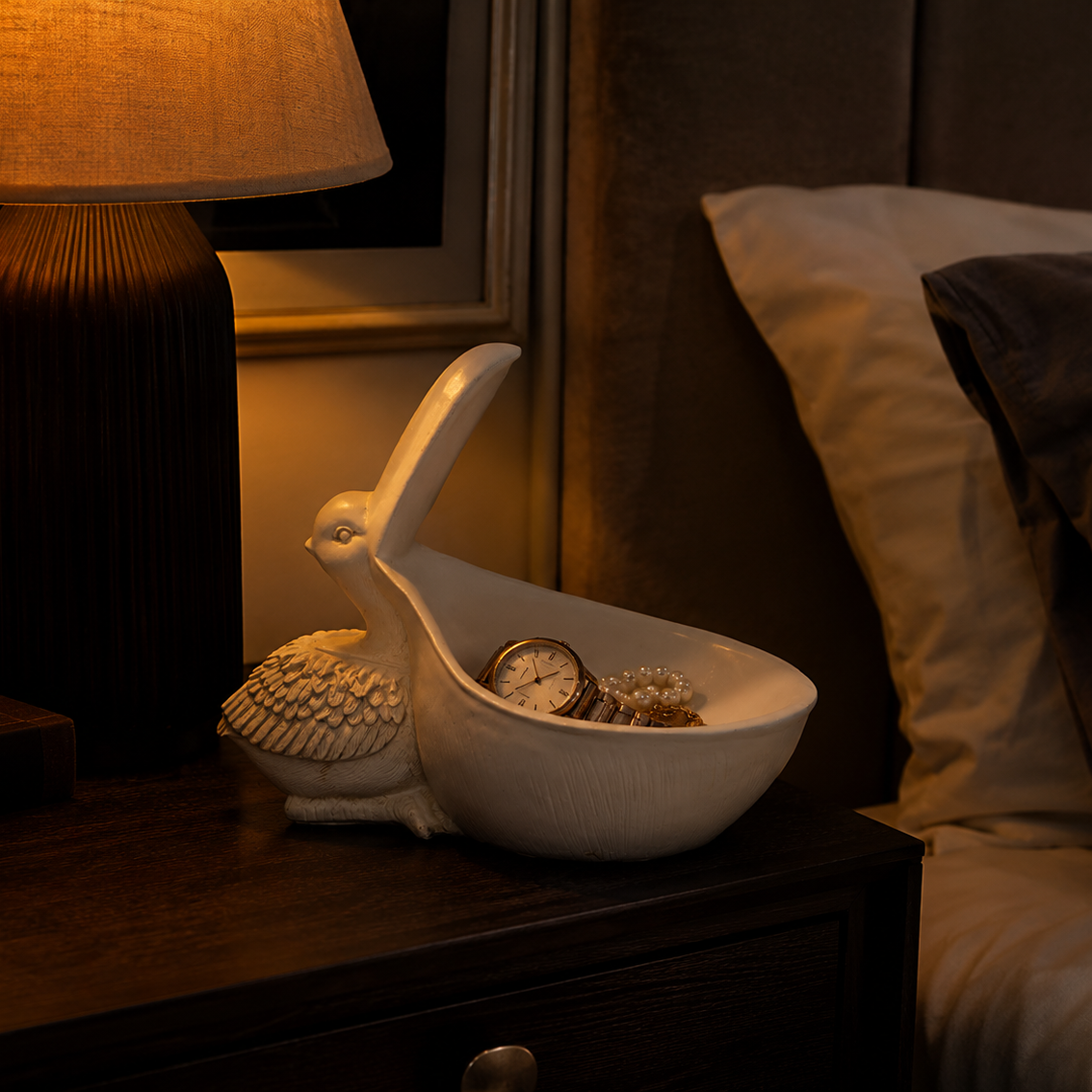 A white ceramic rabbit-shaped bowl tray styled on a dark wooden bedside table next to a lit lamp and bed.