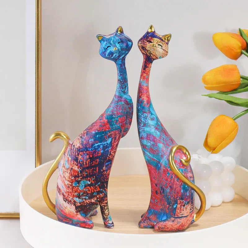 Colorful cat-shaped figurines on a decorative stand with flowers in the background.