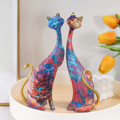 Colorful cat-shaped figurines on a decorative stand with flowers in the background.