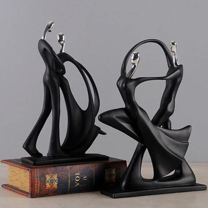 Two black abstract sculptures on a wooden surface with a gray background