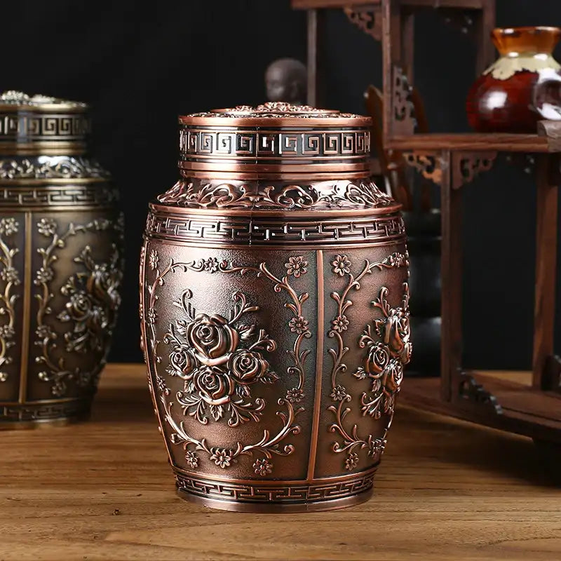 Decorative bronze urn with intricate designs on a wooden surface.