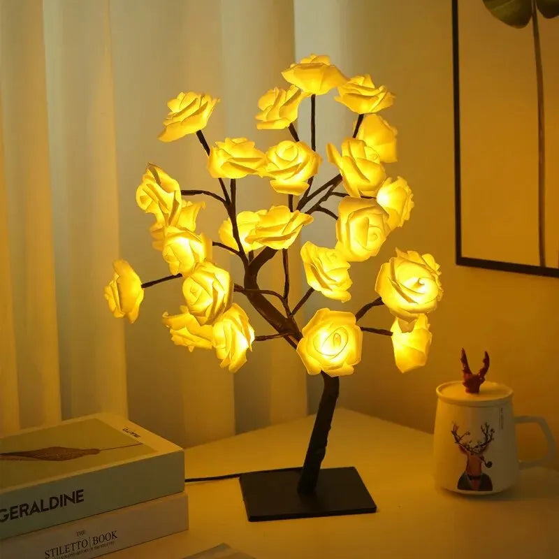 Decorative lamp with illuminated roses on a table next to books and a mug.
