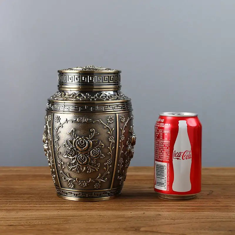 Decorative metal container next to a Coca-Cola can on a wooden surface with a gray background