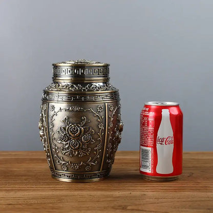 Decorative metal container next to a Coca-Cola can on a wooden surface with a gray background