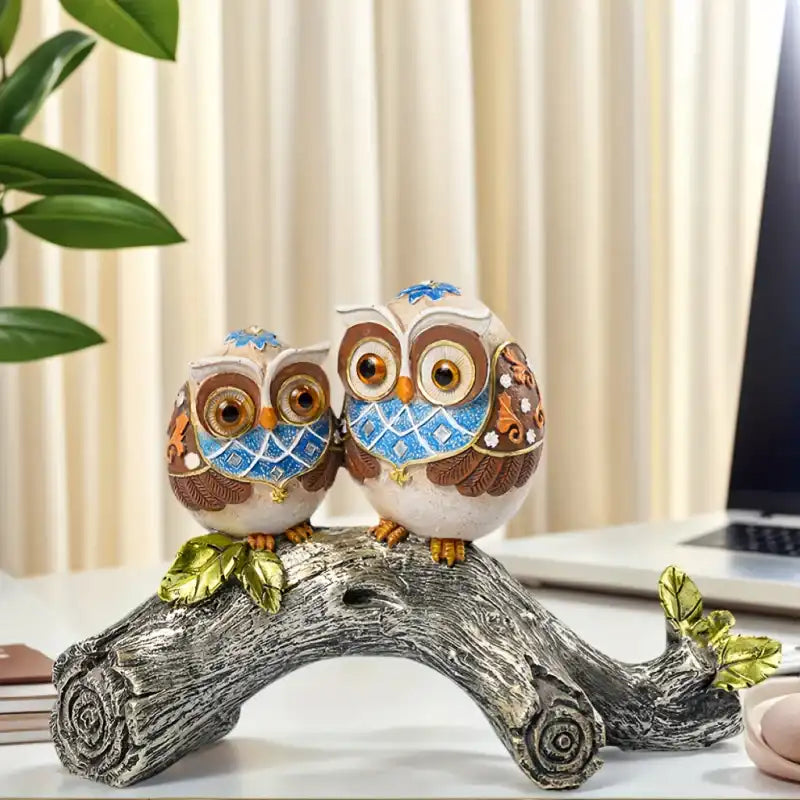 Decorative owl figurine on a branch with a laptop and plant in the background