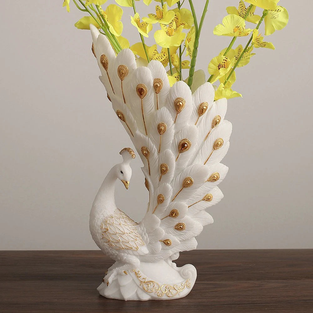 Decorative peacock vase with gold accents holding yellow flowers on a wooden surface.