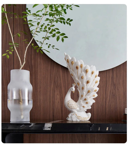 Decorative peacock sculpture on a table with a vase and plant in the background.