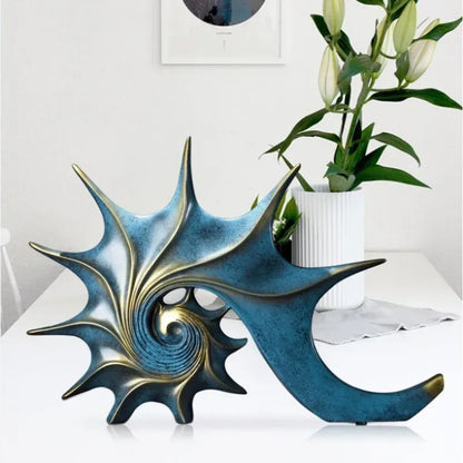 Decorative shell sculpture with spiral design on a white surface, with a plant in the background.