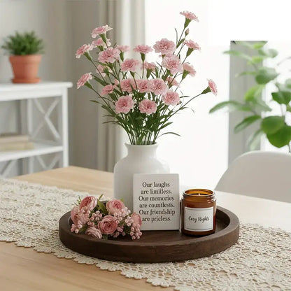 Decorative setup with pink flowers in a vase, a small candle, and a card on a wooden tray.
