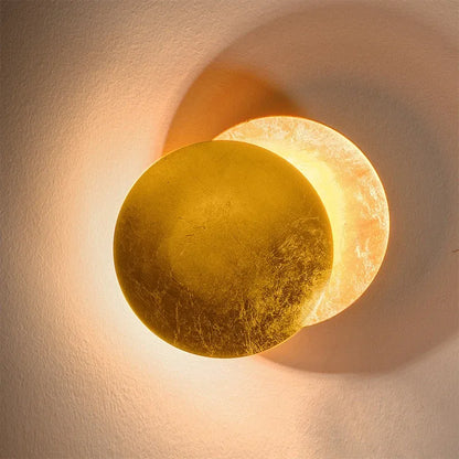 Decorative wall sconce with a gold and beige finish on a textured wall.