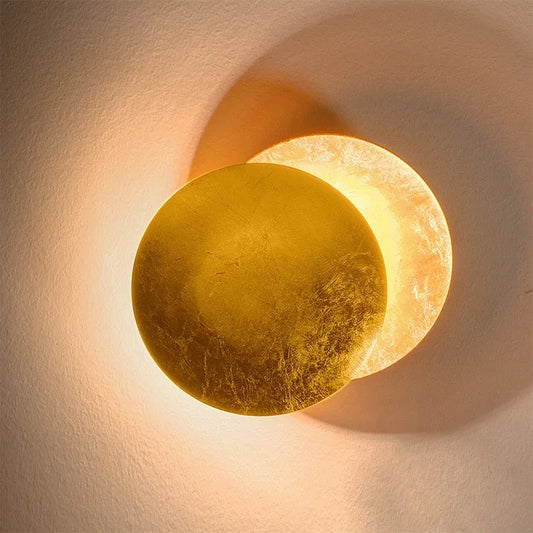Decorative wall sconce with a gold and beige finish on a textured wall.