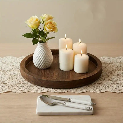 Decorative setting with candles, a vase of flowers, and cutlery on a wooden tray.