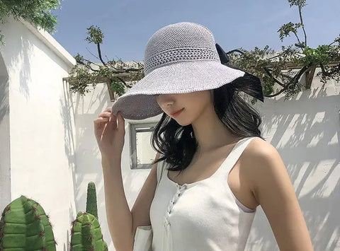 Women's foldable wide-brim beach sun hat lifestyle shot showing bow detail and packable roll-up design
