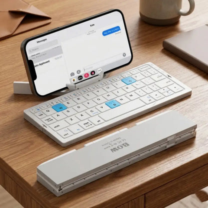 Foldable keyboard attached to a smartphone on a wooden desk with a mug and notebook in the background.