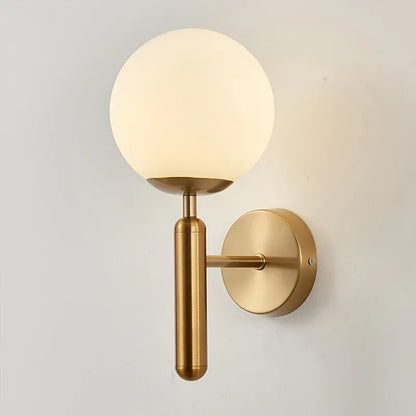 Gold wall sconce with a white globe light on a gray background