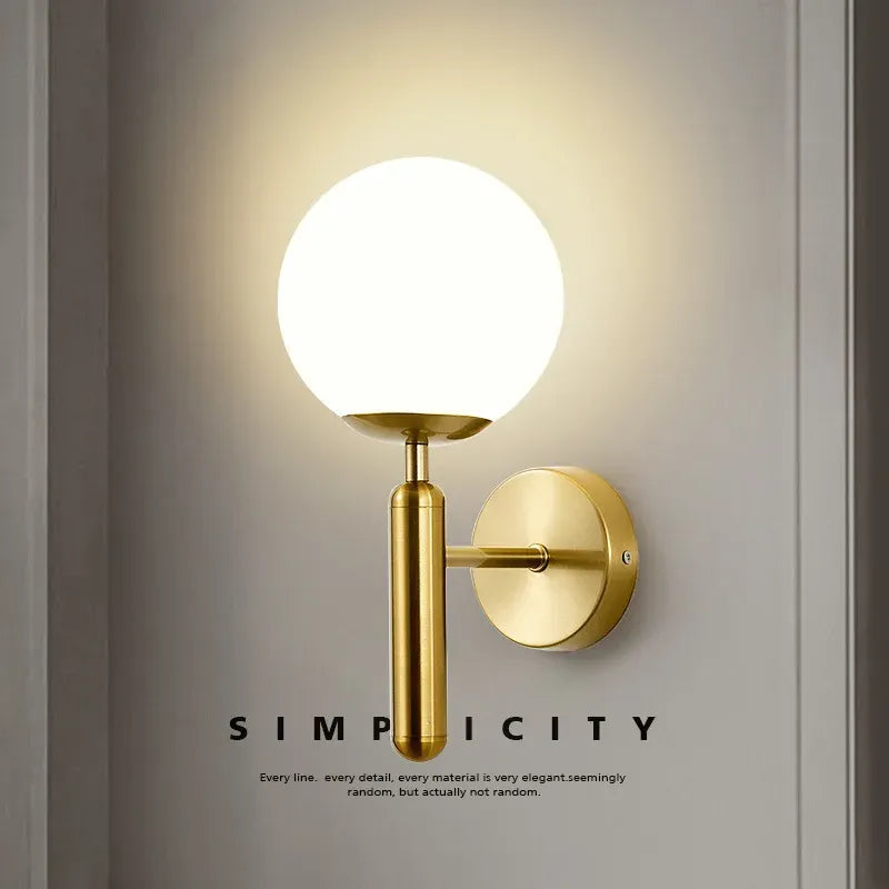 Gold wall sconce with a white globe light on a neutral background, featuring the word 'Simplicity'.