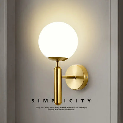 Gold wall sconce with a white globe light on a neutral background, featuring the word 'Simplicity'.
