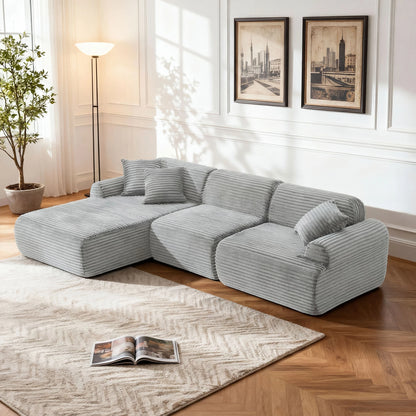Gray sectional sofa in a living room with a plant, lamp, and framed pictures on the wall.
