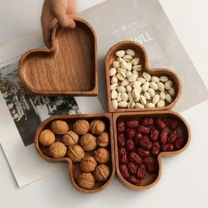 Heart-shaped wooden tray with compartments filled with nuts and dried fruits on a magazine background.
