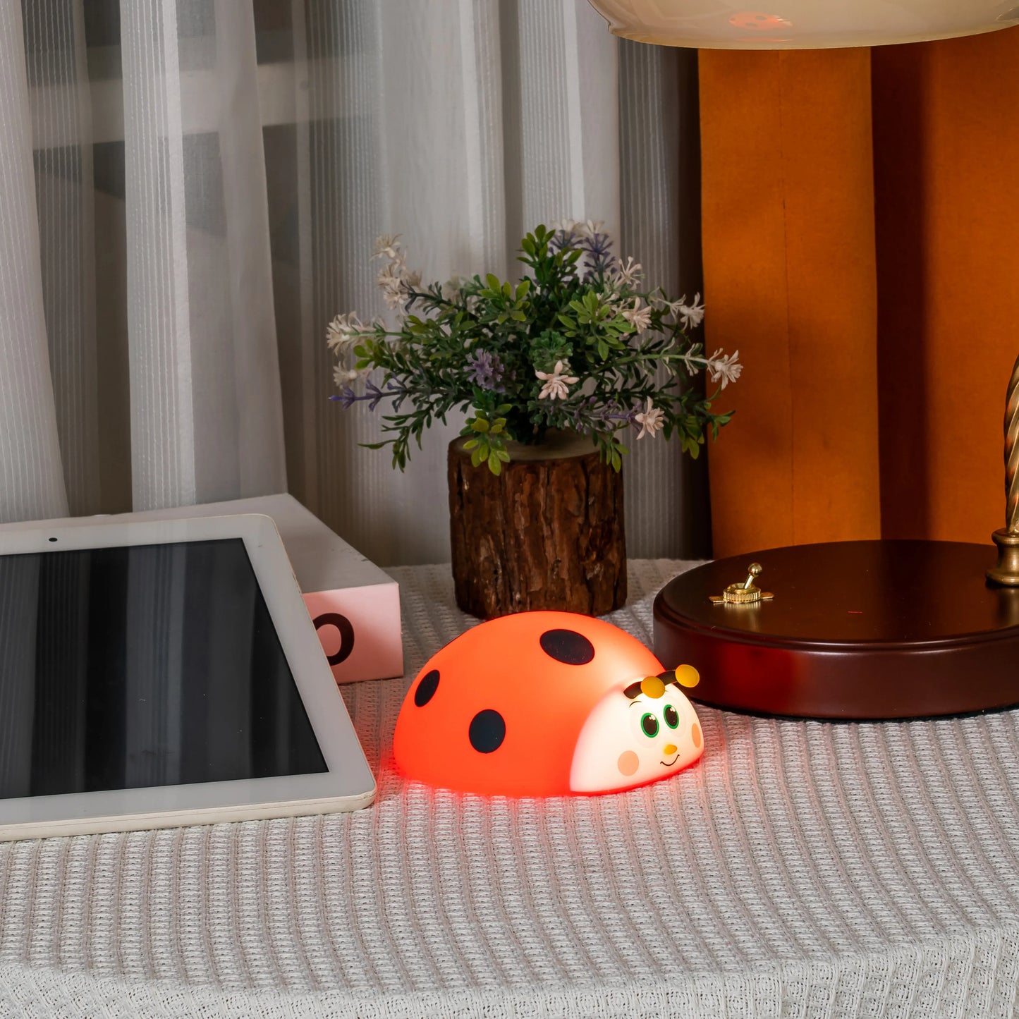 Orange ladybug-shaped night light on a table with a tablet and flowers in the background