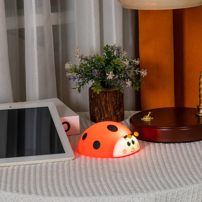 Orange ladybug-shaped night light on a table with a tablet and flowers in the background